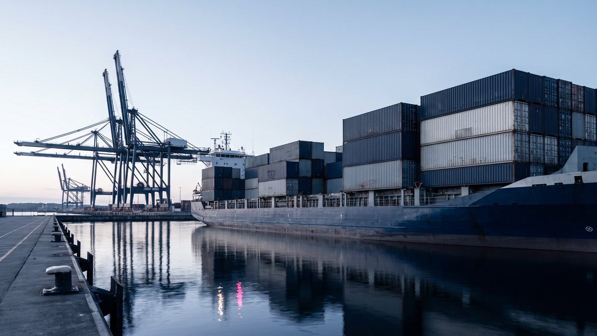 Illustrative container ship moored at an empty quay at dawn beneath two idle ship-to-shore cranes