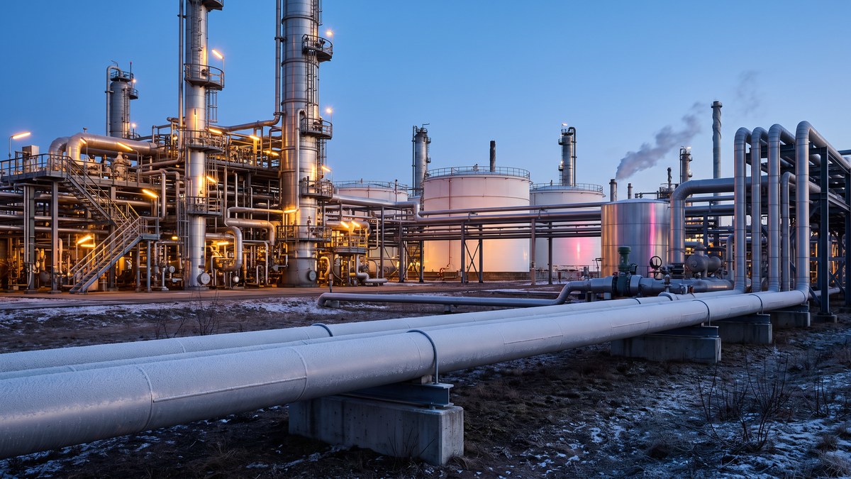 Illustrative oil refinery at winter dusk with distillation columns, storage tanks and a frost-covered pipeline in the foreground
